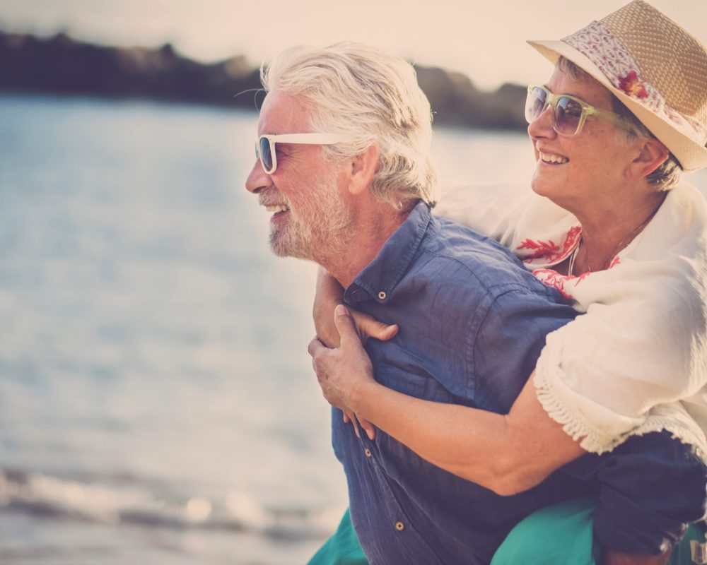 happy senior couple have fun and enjoy outdoor leisure activity at the beach. the man carry the woman on his back to enjoy together a retired lifestyle at the beach